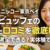 グランドニッコー東京ベイの朝食ビュッフェ会場で、料理を見ながら笑顔のアジア系女性。朝食プレートと共に、評判と口コミを徹底解説するテキストが並ぶ。